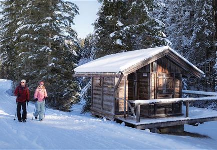 Winterwandern in der Region Seefeld_Mann und Frau laufen neben kleiner Holzhütte im Fludertal.jpg